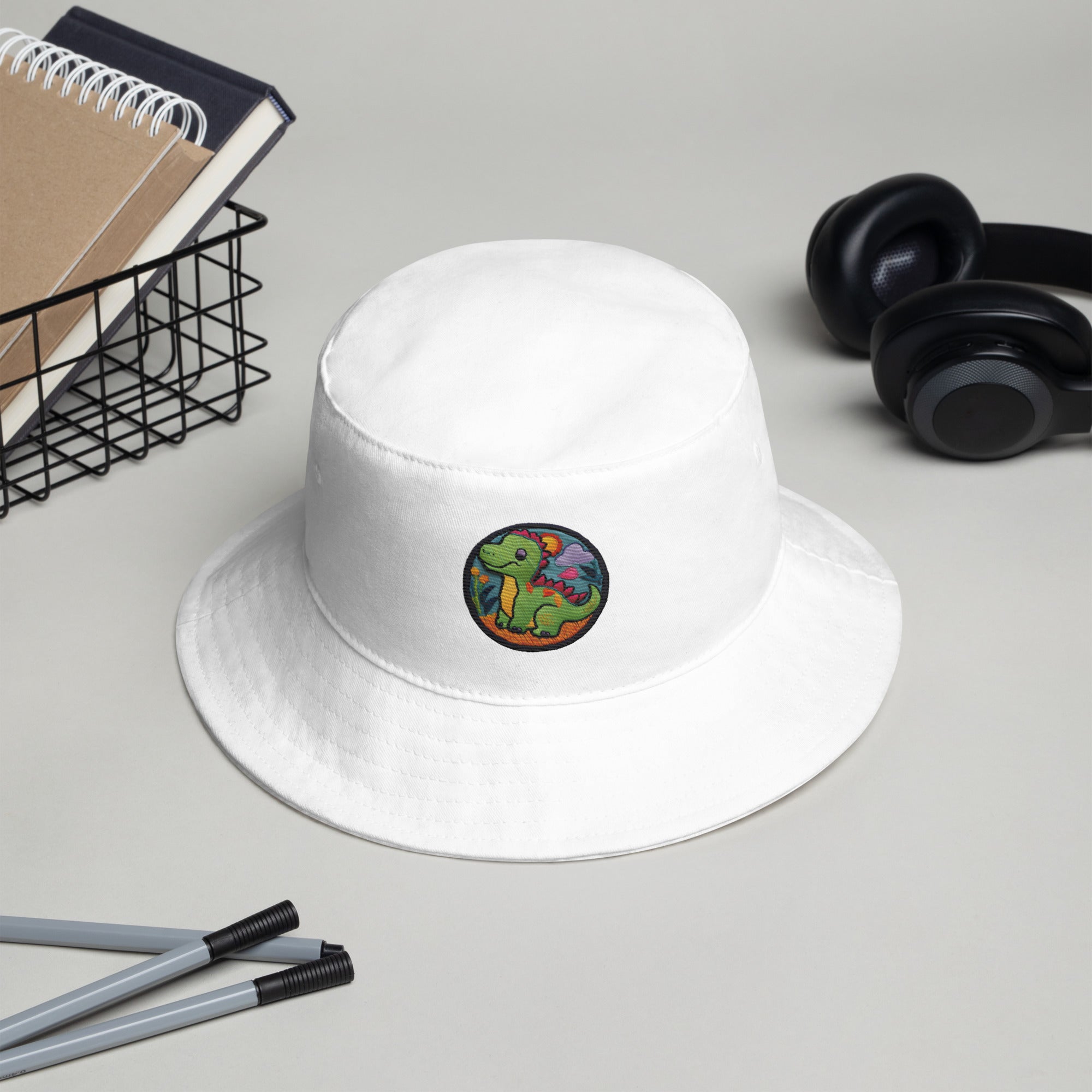 White Dino Dreamer Bucket Hat placed on a desk, showcasing its clean design and potential for personalization.